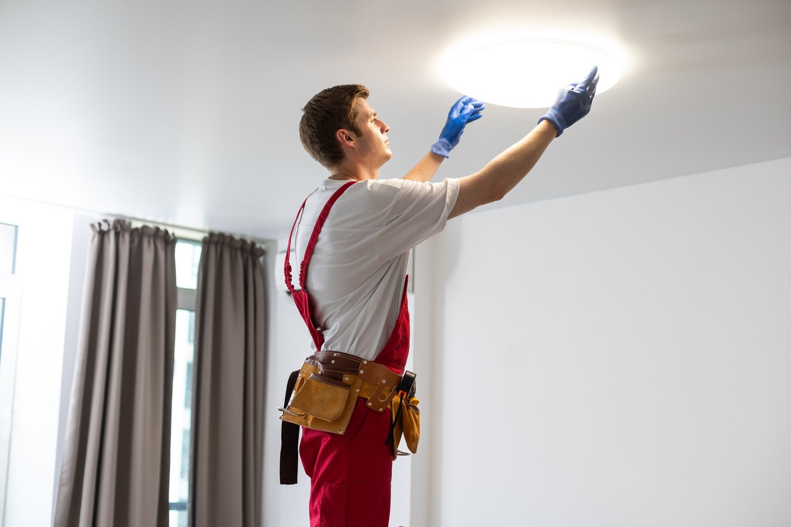 Young man installing ceiling lamp on stepladder in kitchen
